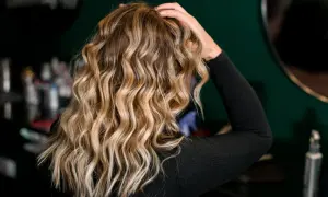 Blond włosy z pięknymi falami, podkreślonymi przez aktywator skrętu włosów. W tle widać kosmetyki fryzjerskie.