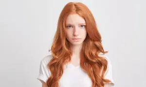 Dziewczyna z burzą rudych włosów, lekko falowanych, patrzy prosto przed siebie.