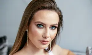 Brązowe włosy pięknie podkreślają niebieskie oczy. Delikatny makijaż i długie kolczyki dodają uroku.