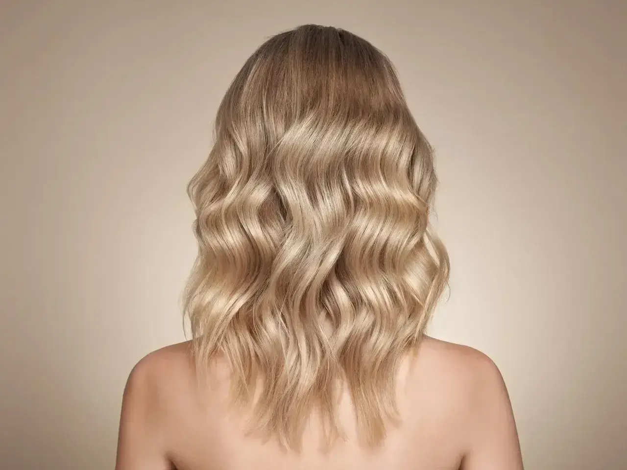 Falujące włosy w odcieniu bezowy blond, delikatnie pofalowane, opadające na ramiona.