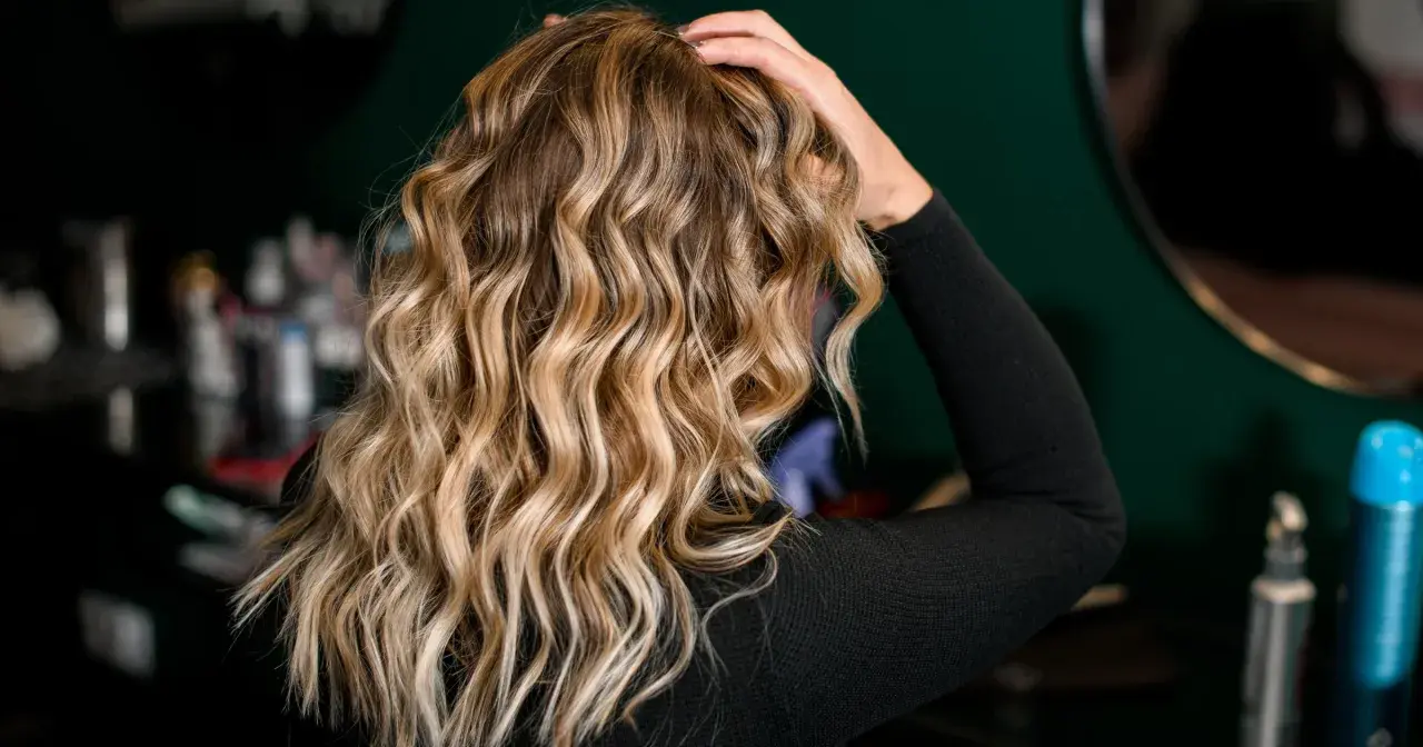 Blond włosy z pięknymi falami, podkreślonymi przez aktywator skrętu włosów. W tle widać kosmetyki fryzjerskie.