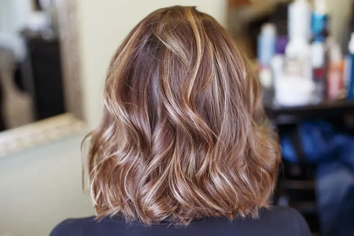 Kobieta z falowanymi włosami w odcieniach brązu i subtelnymi pasemkami blond.