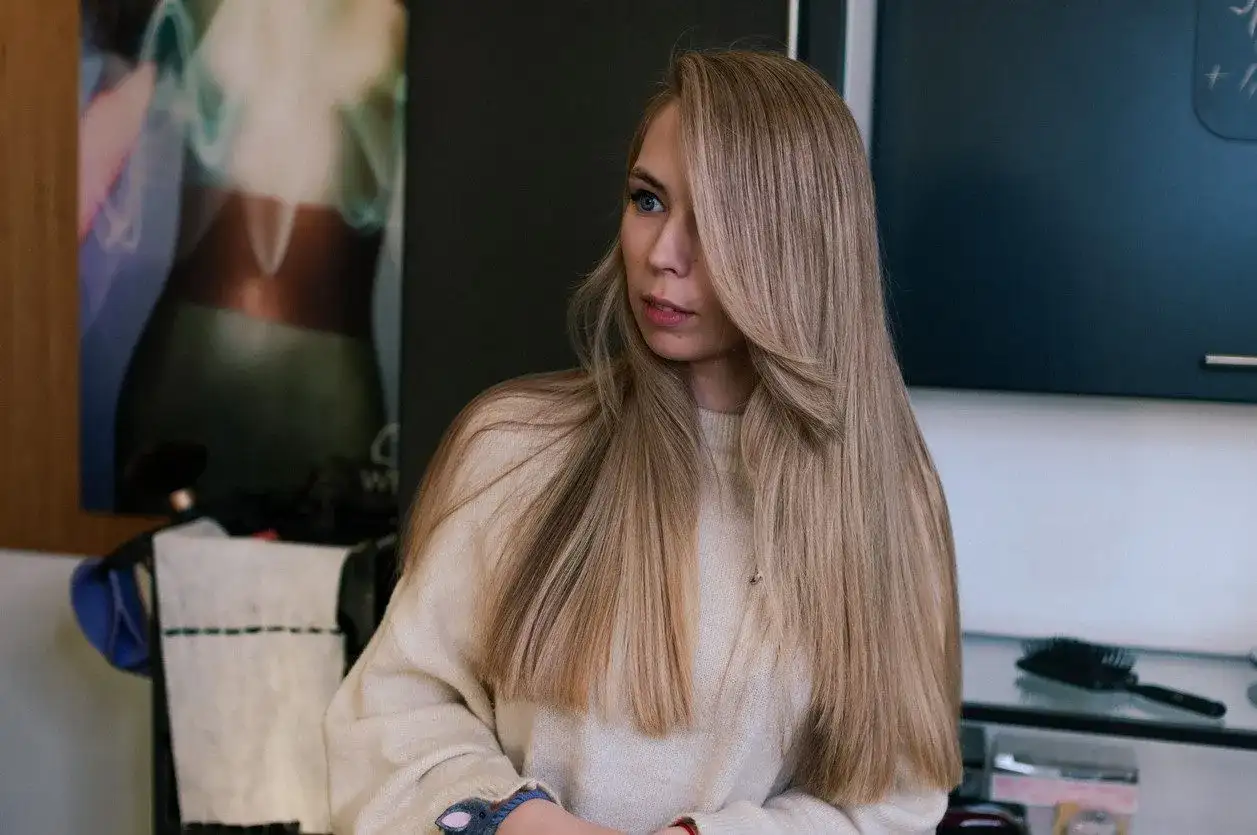 Dziewczyna z długimi, mysi blond włosami, ubrana w beżowy sweter, patrzy w bok.