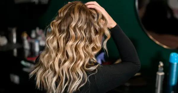 Blond włosy z pięknymi falami, podkreślonymi przez aktywator skrętu włosów. W tle widać kosmetyki fryzjerskie.
