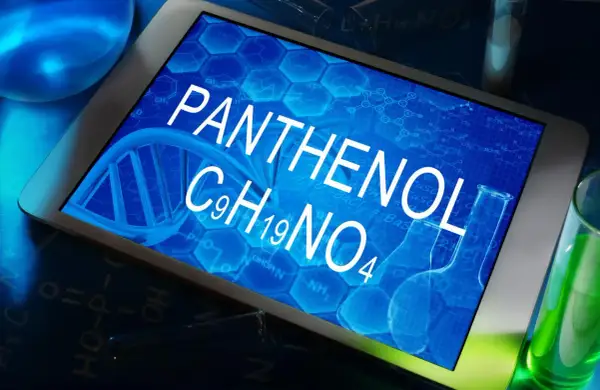 Tablet z napisem PANTHENOL i wzorem chemicznym C9H19NO4, otoczony probówkami z zielonym płynem i elementami chemicznymi.